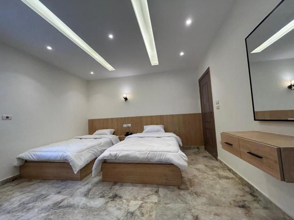 A bedroom with two single beds, a wooden headboard, a marble floor, a wooden dresser, and a wall-mounted mirror.