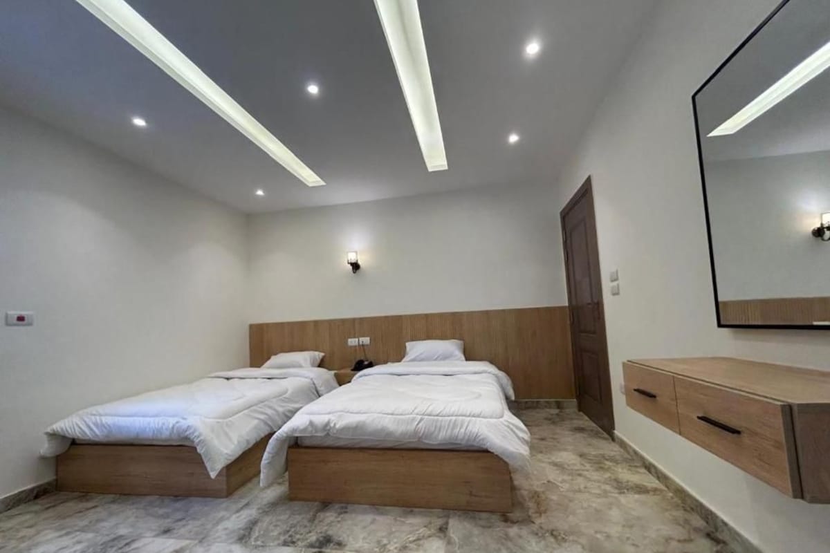 A bedroom with two single beds, a wooden headboard, a marble floor, a wooden dresser, and a wall-mounted mirror.