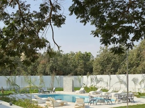 A swimming pool area with lounge chairs and tables, surrounded by greenery and a white wall. - Nakhil Pyramids Resort (Giza)