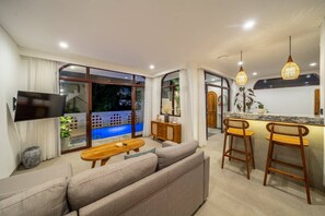 A modern living room with a sofa, a TV, and a pool view. - 3BR Private Pool Villa with Rooftop in Pererenan Near Canggu (Pererenan)