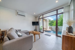 A modern living room with a grey sofa, a wooden coffee table, and a TV mounted on the wall. - 3BR Private Pool Villa with Rooftop in Pererenan Near Canggu (Pererenan)