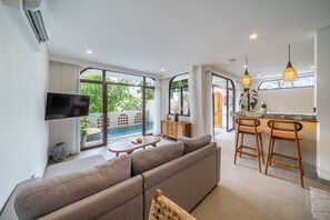 A modern living room with a large sofa, a TV, and a dining area with bar stools. - 3BR Private Pool Villa with Rooftop in Pererenan Near Canggu (Pererenan)
