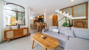 Een moderne woonkamer met een bank, een houten salontafel en een eethoek met stoelen.