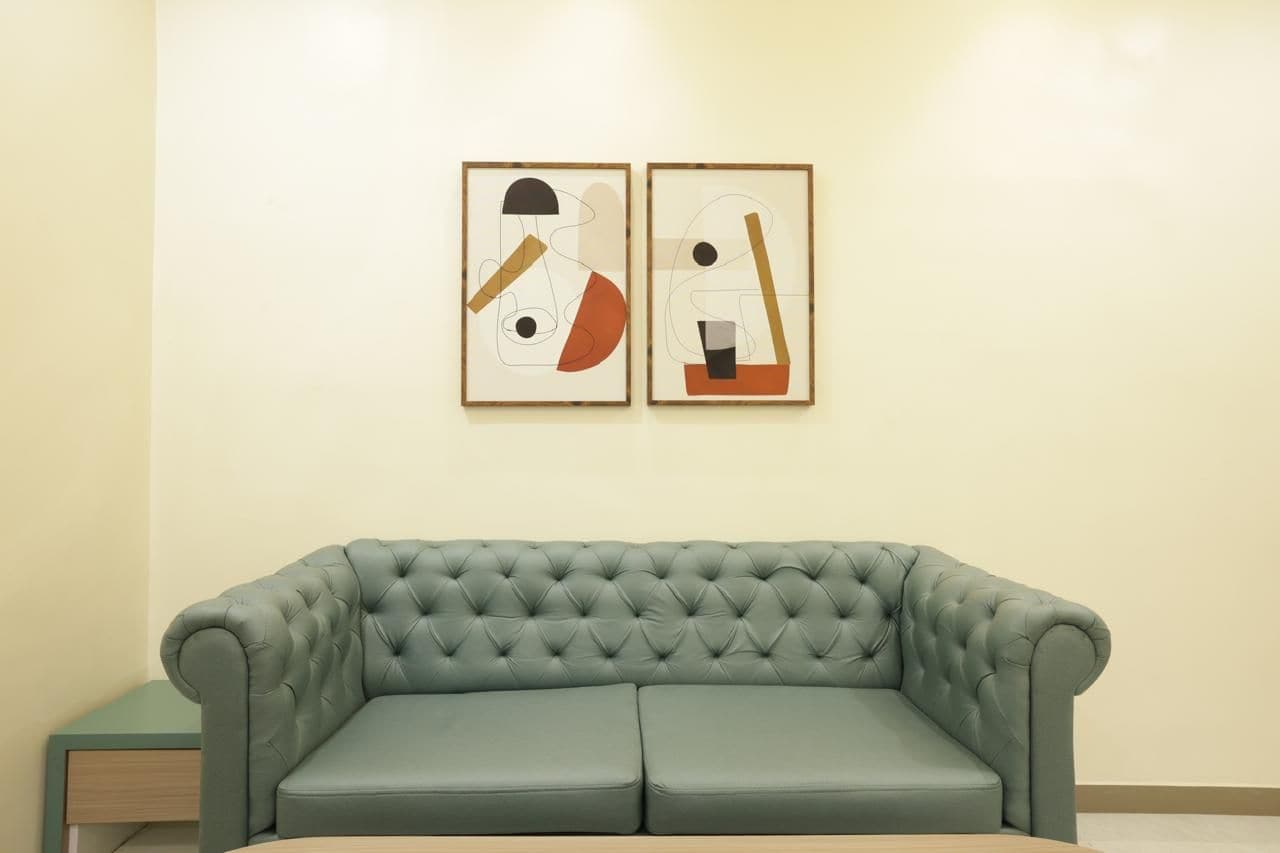 Una habitación con un sofá verde con capitoné y dos cuadros abstractos en la pared.