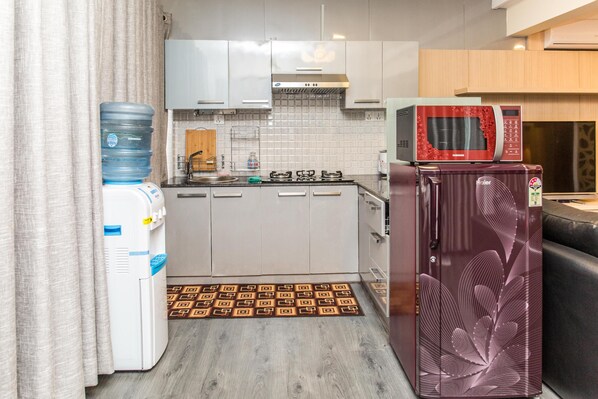 Cozinha compacta com armários brancos, micro-ondas, geladeira, dispensador de água e tapete estampado.