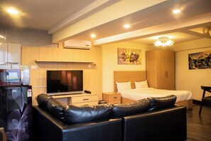 Quarto de hotel moderno com cama, televisão, frigorífico, sofá e um quadro na parede.