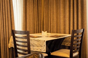 Uma mesa de jantar com toalha de renda, duas cadeiras de madeira e um livro sobre a mesa.