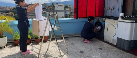A rooftop with a washing machine and a drying rack, surrounded by potted plants.