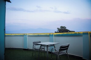 Terraço no telhado com mesa e cadeiras, vista para montanhas ao longe e parede azul com luzes amarelas.