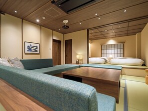 A modern hotel room with a sofa, a bed, a wooden coffee table, and a wall-mounted projector. - Imagasa-so, Osaka, Tempozan — Fish Merchant — (大阪市港区築港4丁目)