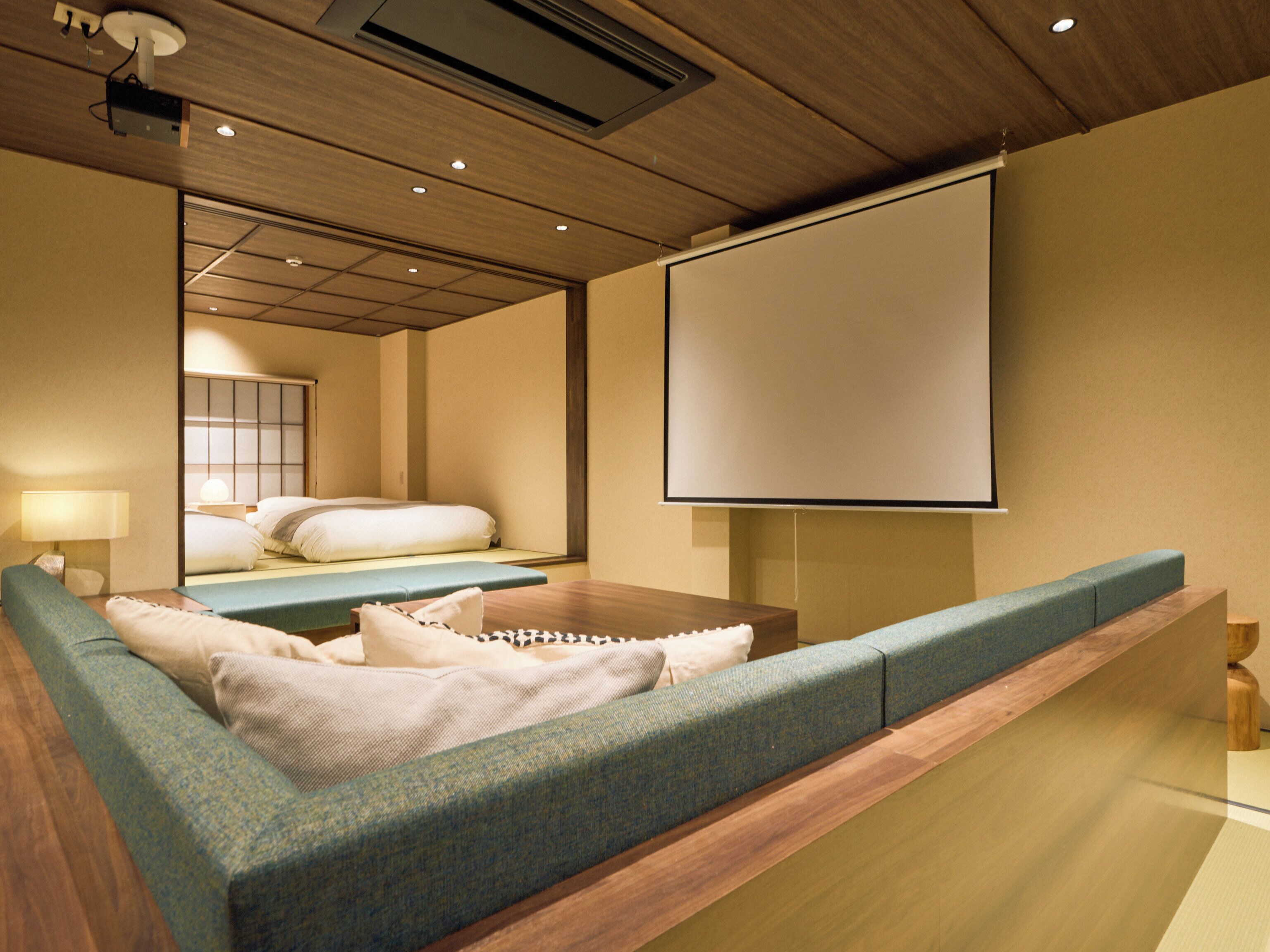 A modern hotel room with a large bed, a seating area, a flat-screen TV, and a ceiling projector.