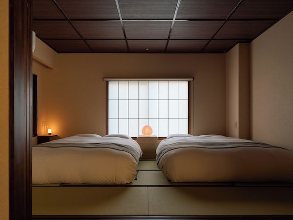 A traditional Japanese room with tatami flooring, a sliding shoji screen window, and two beds with pillows.