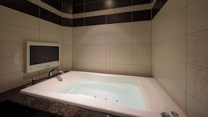 Un baño con una bañera independiente, un televisor montado en la pared y una encimera de mármol.
