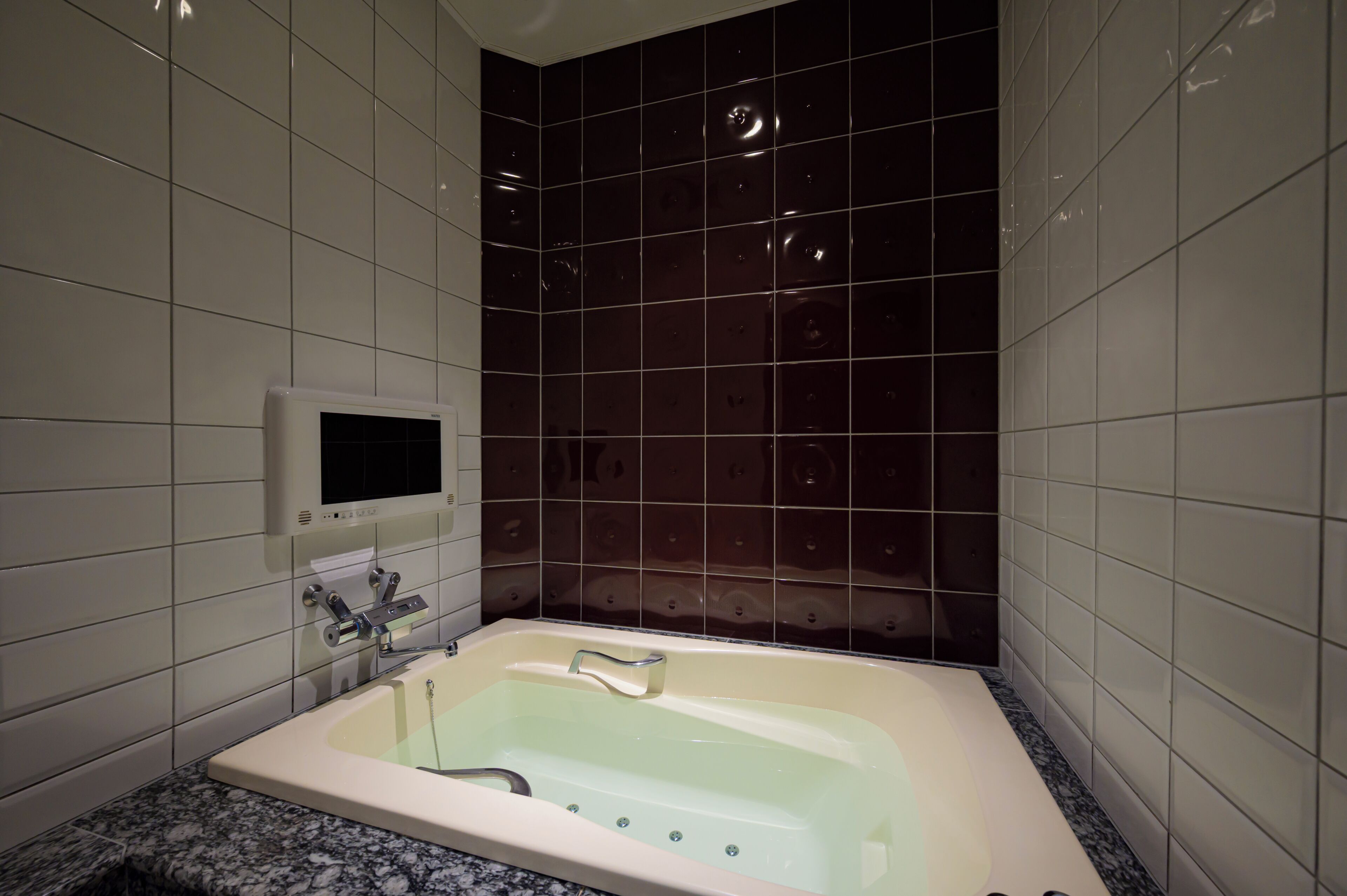 A bathroom with a bathtub, a hand dryer, and a wall-mounted control panel.