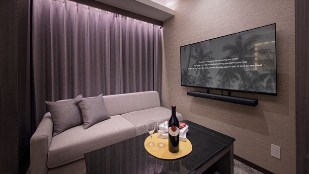 A modern hotel room with a sofa, a flat-screen TV mounted on the wall, and a table with a bottle of wine and glasses. - HOTEL TWIN FLAG (Ichikawa)