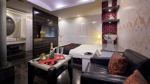 Una habitación de hotel moderna con cama, sofá, una mesita con una botella y vasos, un cuenco decorativo y una pared con estampado floral.