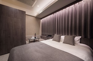 Una habitación de hotel moderna con una cama grande, una mesita de noche, una pequeña mesa con una botella y vasos, y un armario.