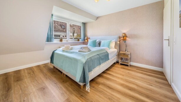 Ein Schlafzimmer mit einem Bett, Nachttischen, einem Fenster mit Vorhängen und einer Deckenleuchte.