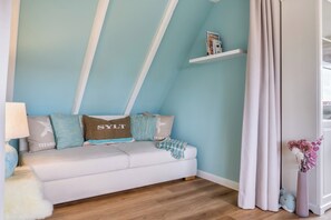 Una habitación con un sofá blanco, una lámpara, una estantería con libros y una cortina.