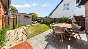 Eine Terrasse mit einem Holztisch und Stühlen, einer Backsteinmauer und einem Holzzaun.