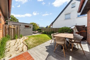A patio with a wooden table and chairs, a brick wall, and a wooden fence. - Modern 3-room vacation apartment with approximately 75 m² of living space, accommodating up to 6 people (Wenningstedt-Braderup (Sylt))
