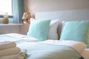 A neatly made bed with a white and light blue duvet, two pillows, and a bedside lamp on a textured wall. - Modern 3-room vacation apartment with approximately 75 m² of living space, accommodating up to 6 people (Wenningstedt-Braderup (Sylt))