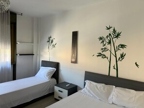 A hotel room with two beds, a nightstand, a wall-mounted artwork, and a window with curtains. - Two-Bedroom Family Apartment (Venezia)