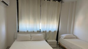 Een slaapkamer met een groot bed, een kleiner bed, een nachtkastje en een stoel.