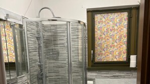 Een badkamer met een glazen douchecabine, een witte wastafel, een toilet en een raam met een kleurrijk patroon.