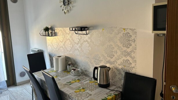 Een eethoek met een tafel gedekt voor twee personen, een wandklok, een aan de muur bevestigde televisie en behang met een patroon.