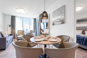 Una habitación de hotel moderna con una mesa redonda de comedor, asientos cómodos, un televisor de pantalla plana y obras de arte en las paredes.