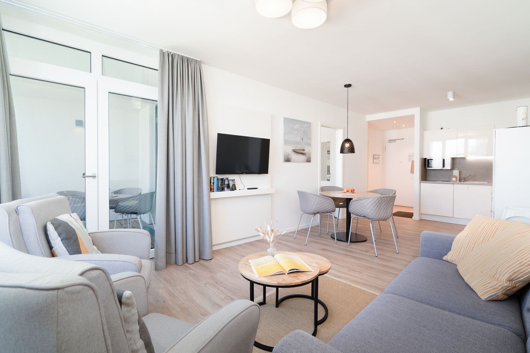 A modern living room with a sofa, chairs, a coffee table, a TV, and a dining area with chairs and a table.