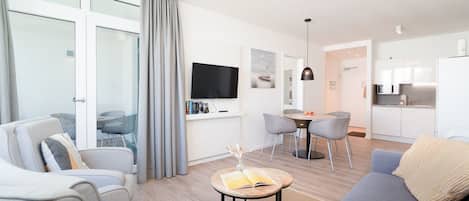 A modern living room with a sofa, chairs, a coffee table, a TV, and a dining area with chairs and a table.