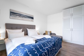 Una cama bien tendida con ropa de cama blanca y azul, un cabecero gris y una manta estampada azul.