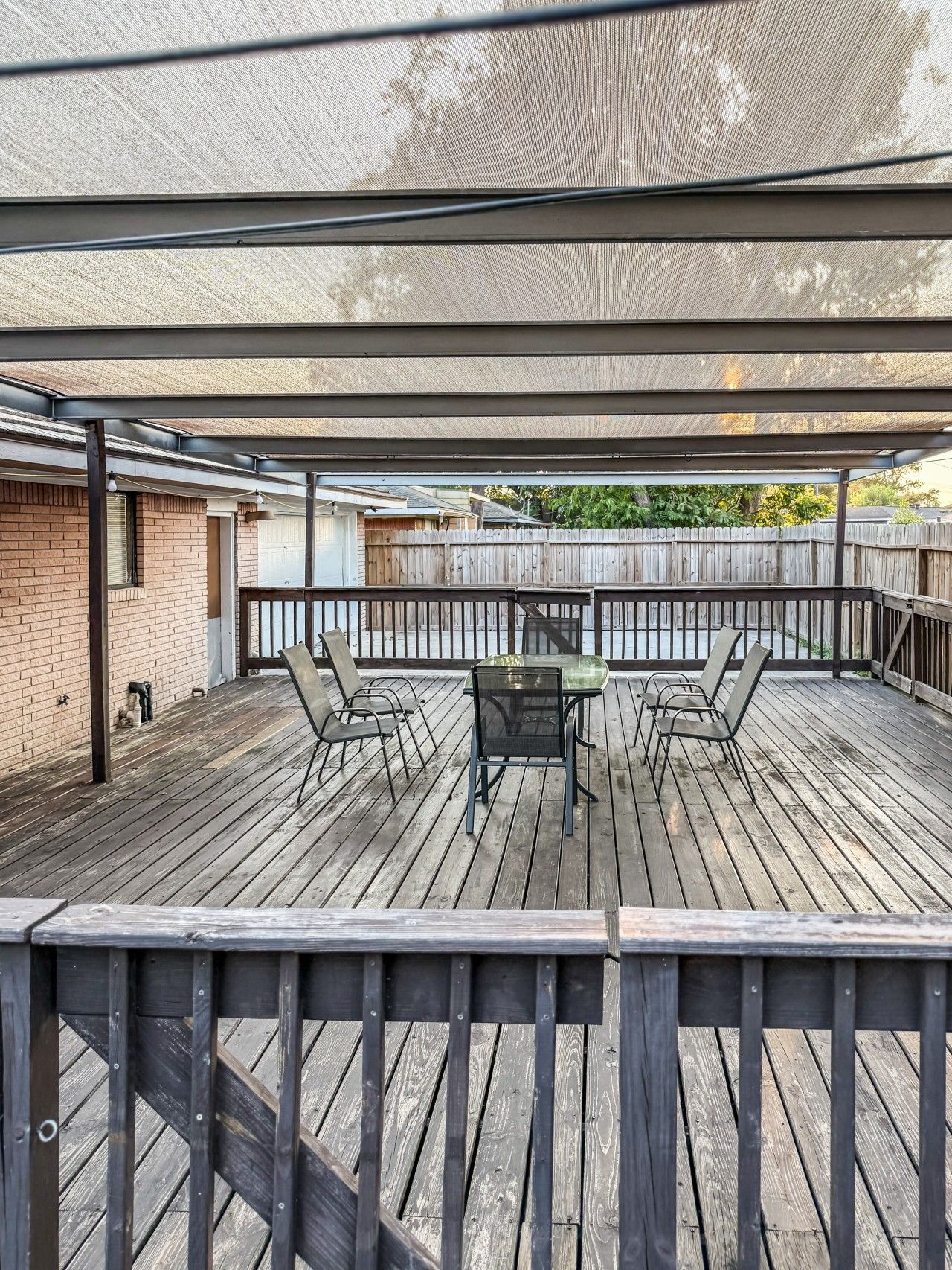 Terrassa exterior coberta amb taula i cadires, un pont de fusta i vista a una zona residencial.