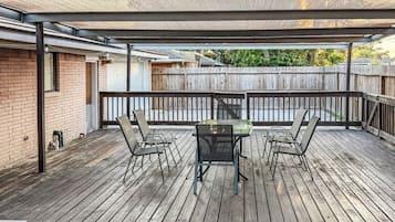 En täckt uteplats med ett bord och stolar, ett trädäck och utsikt över ett bostadsområde.