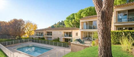 A residential building with a swimming pool, a balcony, and a tree in the foreground.