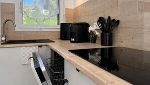 A modern kitchen with a dishwasher, a coffee maker, and a window with a view of greenery. - ALBIZIA Residence: 1-Bedroom Apartment with Spa, Pool, and Parking - Renovated in 2026 (Gréoux-les-Bains)