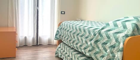 Un dormitori amb un llit, un taulell de fusta i una finestra amb cortines.