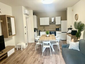A compact living space with a dining area, kitchenette, and a seating area with a sofa and a TV. - Sirmione Brema Wave House with Garden—Near the Lake (Sirmione)