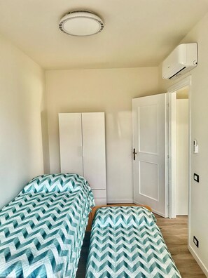 A bedroom with two beds, a wardrobe, a door, and an air conditioning unit. - Sirmione Brema Wave House with Garden—Near the Lake (Sirmione)