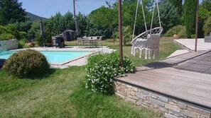 A backyard with a swimming pool, a wooden deck, and a hanging chair. - Villa Dolce Vita (Nans-les-Pins)