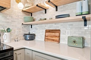 A kitchen with white subway tiles, wooden shelves, a slow cooker, a toaster, and a cutting board. - A Sea View: Modern Coastal Luxury | 2BR/2BA with Ocean Views (Surf City)