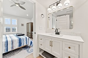 A bedroom with a bed, a bathroom with a sink and mirror, and a ceiling fan. - A Sea View: Modern Coastal Luxury | 2BR/2BA with Ocean Views (Surf City)