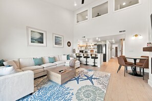 A modern living room with a sofa, coffee table, and a dining area with chairs. - A Sea View: Modern Coastal Luxury | 2BR/2BA with Ocean Views (Surf City)