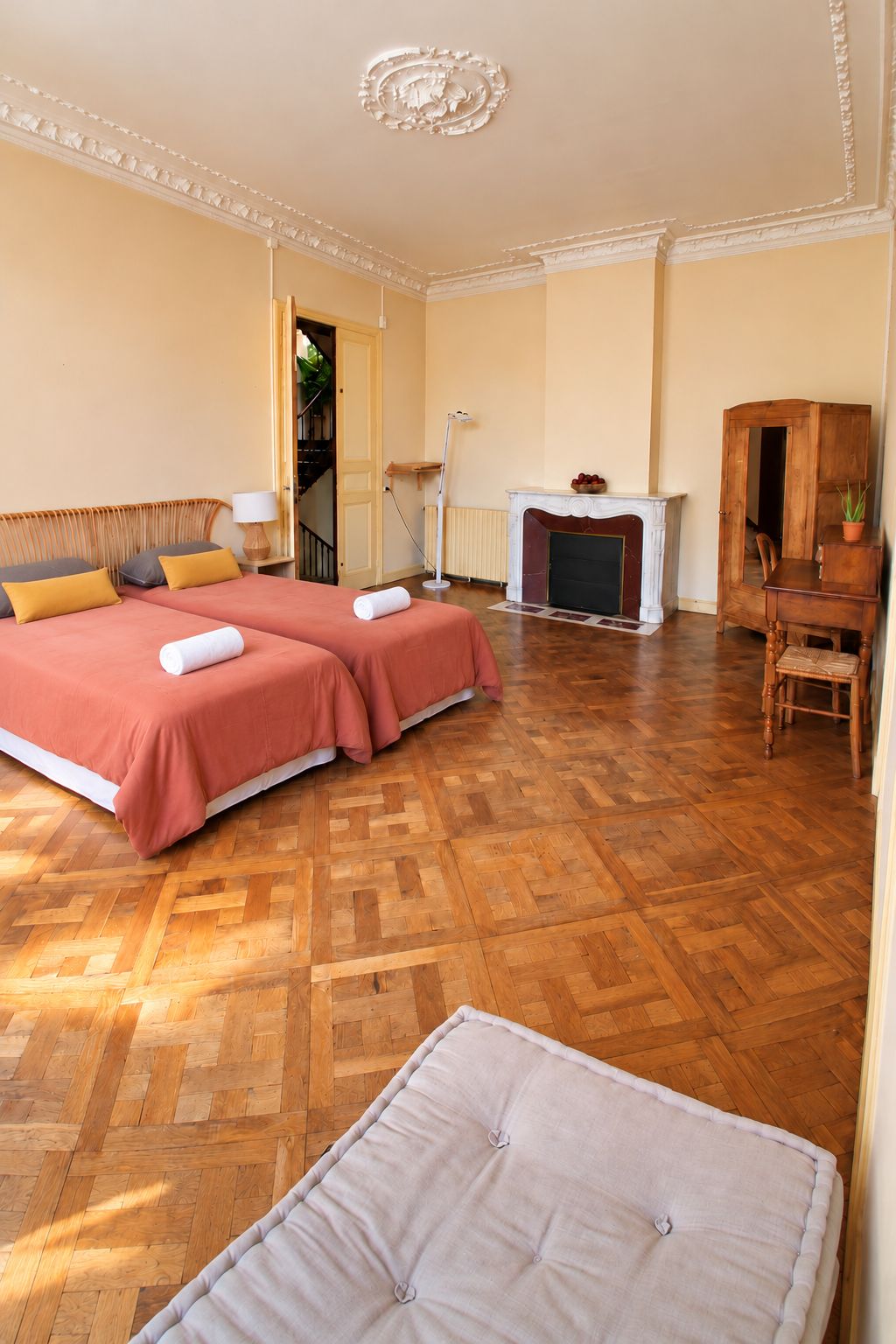 Quarto de hotel com cama de casal, área de estar com uma poltrona e uma mesa, lareira e piso de madeira.