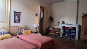 Ein Zimmer mit zwei Betten, einem kleinen Tisch, einem Stuhl, einem Kamin und einer Tür zu einem anderen Raum.
