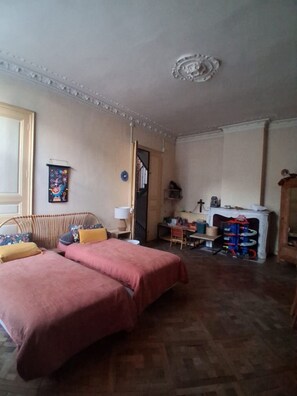 Ein Zimmer mit zwei Betten, einem kleinen Tisch, einem Stuhl, einem Kamin und einer Tür zu einem anderen Raum.