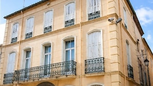 Ein mehrgeschossiges Gebäude mit einer symmetrischen Fassade, großen Fenstern mit Fensterläden und einem zentralen Eingang mit einer Tür.