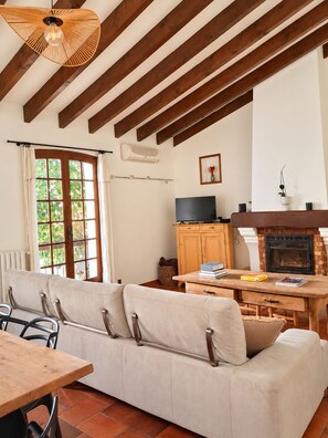 A living room with a sofa, a wooden table, a TV, and a fireplace. - Maison Sarava – Charming apartment with balconies and spacious rooms (Espira-de-l'Agly)